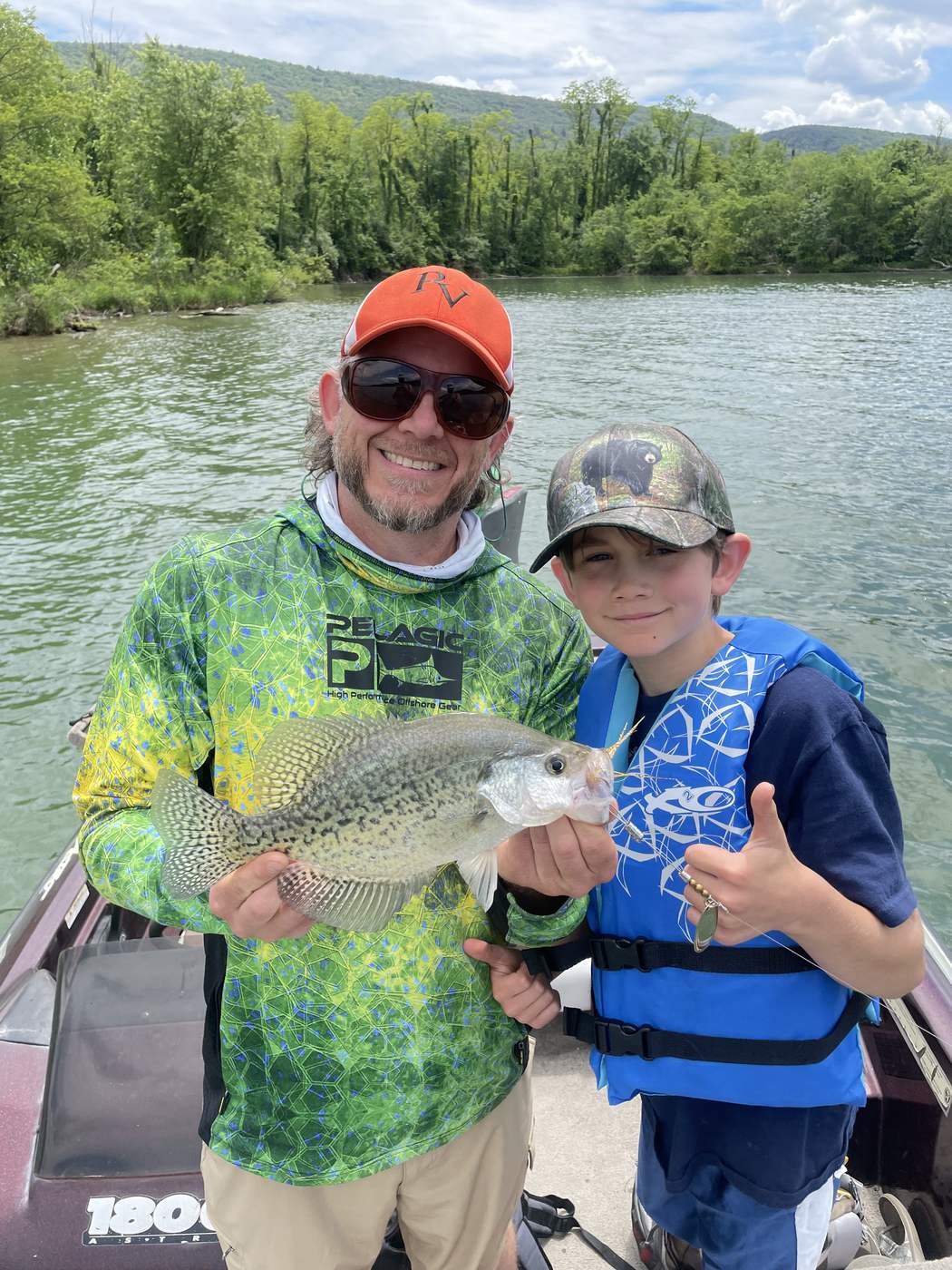 A white crappie held up from a boat with the gold blade of a Timberwolf spinner hanging below it.