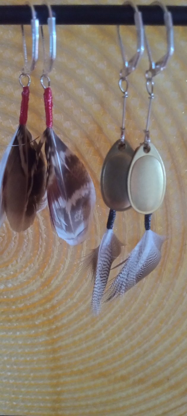 Close-up of Timberwolf earrings pairing polished spinner blades with barred feathers.